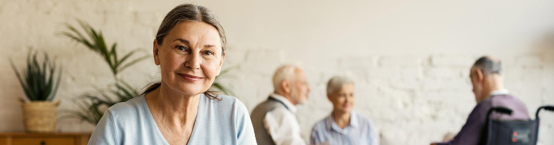 A woman smiling with three individuals sitting in the background.