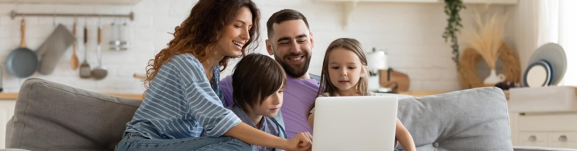 Parents and two children sitting on a couch and looking at a laptop screen. 